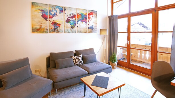 A living room with a sofa, a coffee table, and a chair. There is a window with curtains, a lamp, and a plant. - MyWinkl-Design-Ferienwohnungen  (Reit im Winkl)