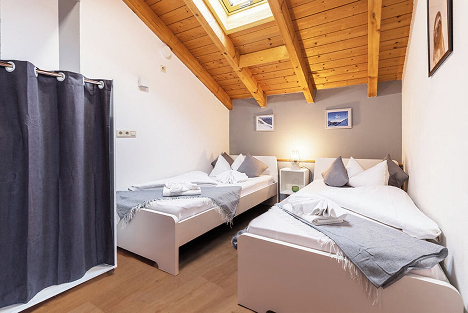 Una habitación con dos camas, cortina de ducha, vigas de madera en el techo y una mesita de noche con lámpara.