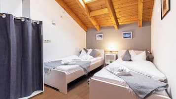 Una habitación con dos camas, cortina de ducha, vigas de madera en el techo y una mesita de noche con lámpara.