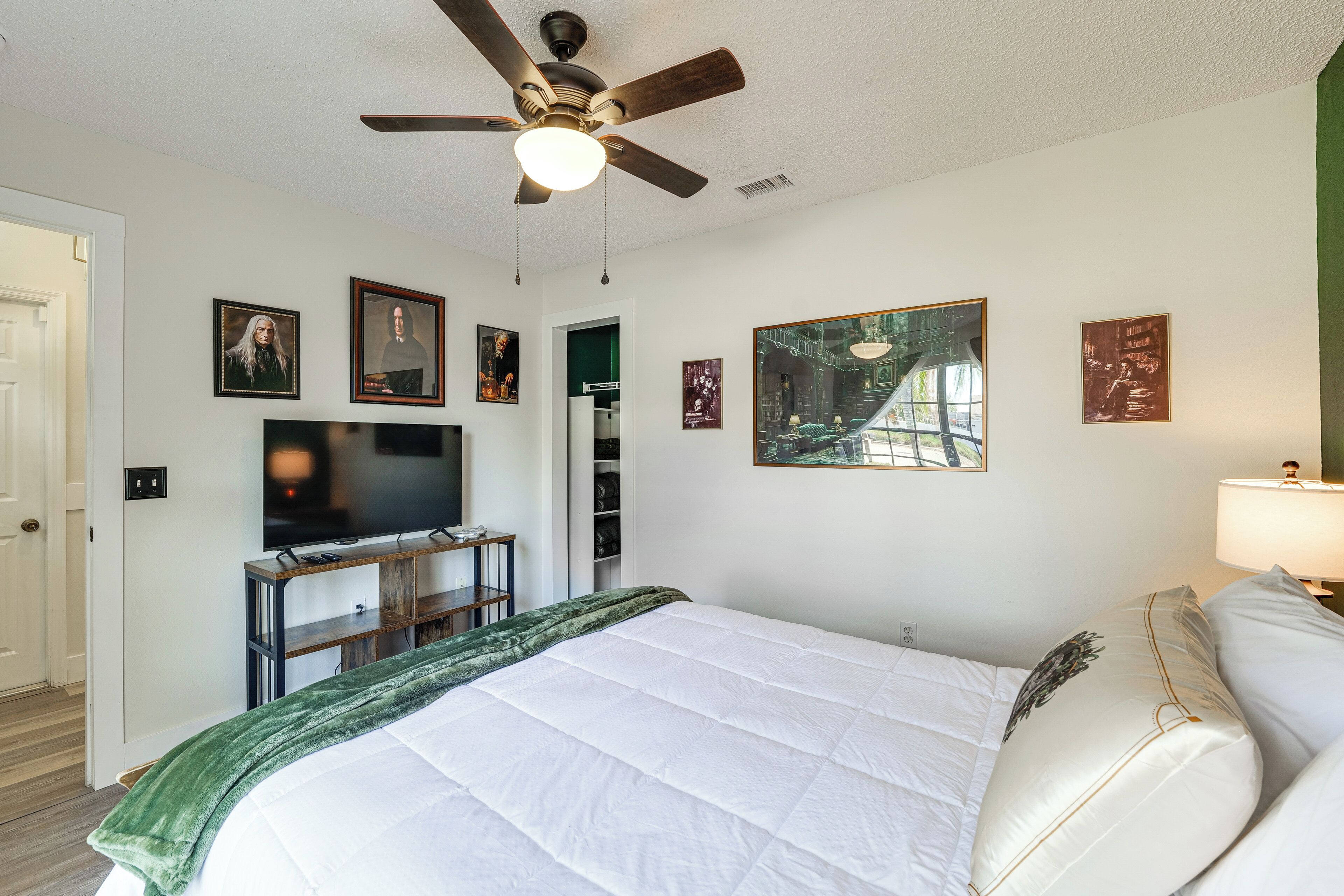 A bedroom with a bed, a ceiling fan, a TV, and framed pictures on the wall.