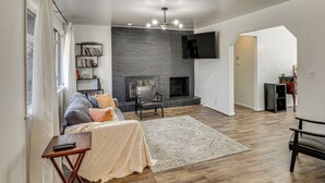 A living room with a fireplace, a bookshelf, and a television mounted on the wall. - 3 Mi to Geha Field at Arrowhead: Easy Match Access (Independence)