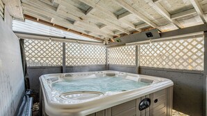 Ett bubbelbad under en träpergola med ett spaljéliknande bakstycke.