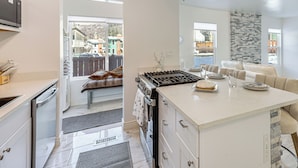 A modern kitchen with white cabinetry, a central island, and a view of a backyard with a wooden deck and a house. - Newly Renovated, Modern Mtn Getaway: Pets Welcome! (Vail)