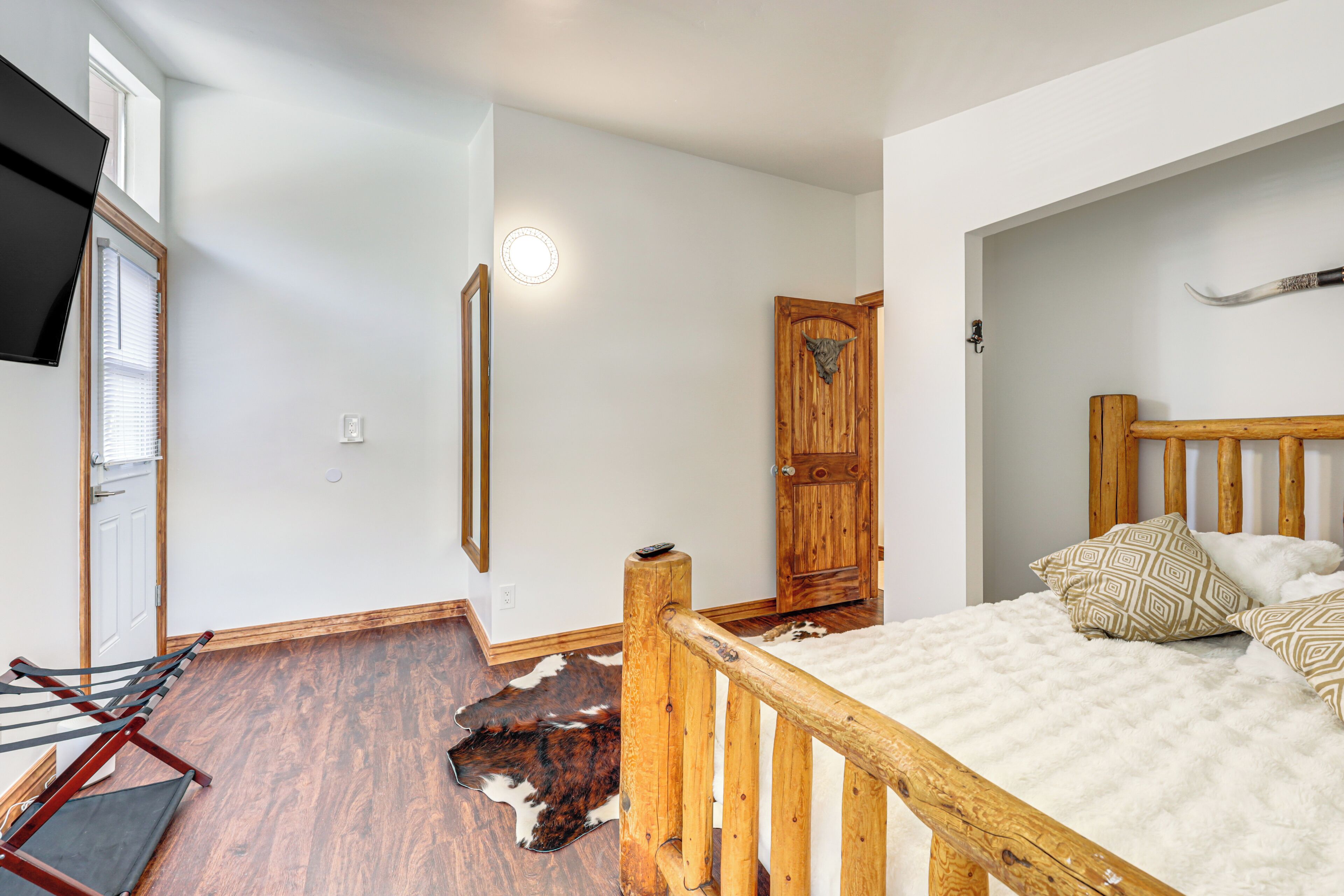 Une chambre avec un lit en bois, un tapis en peau de vache et une porte en bois.