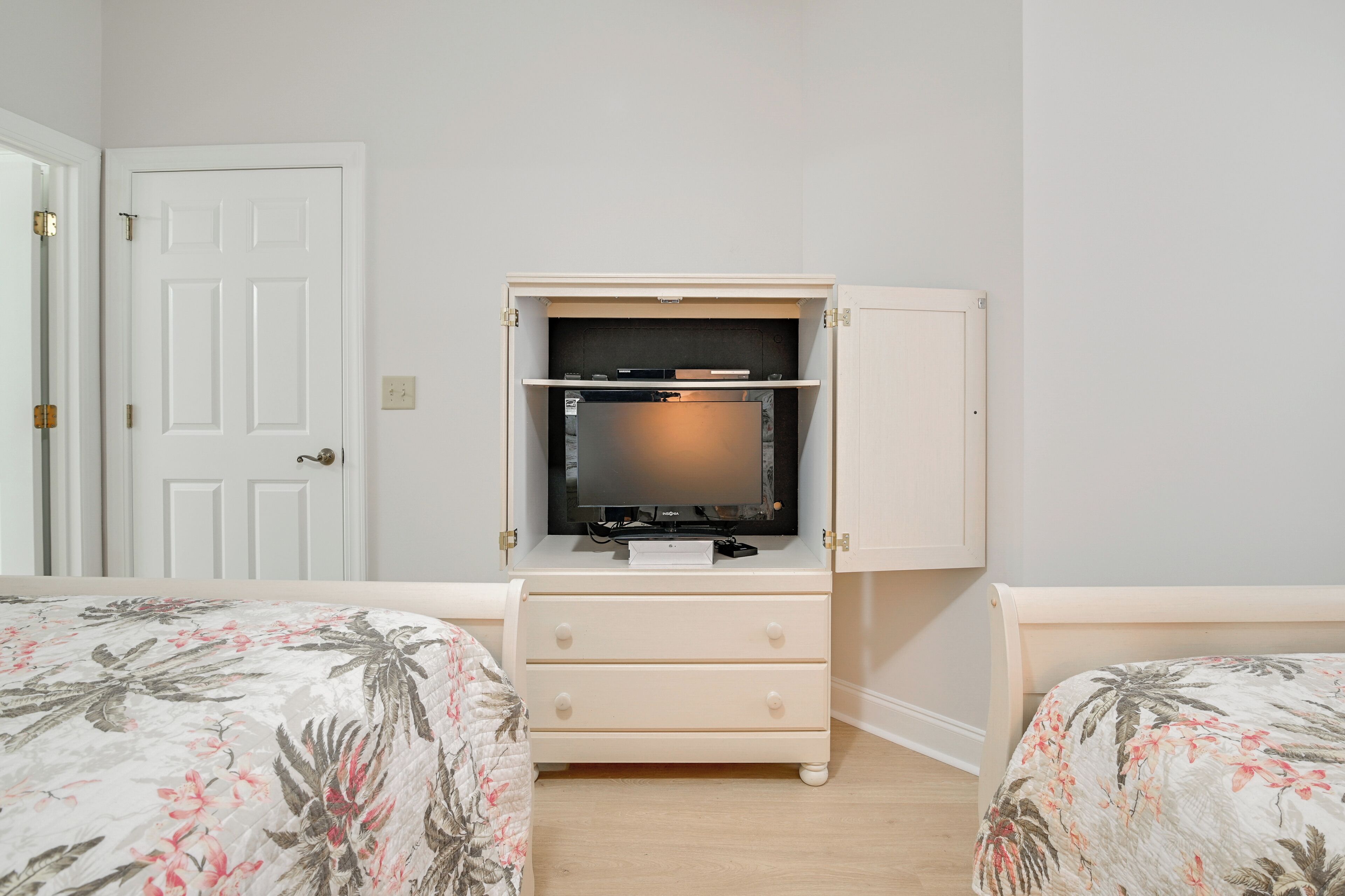 Quarto com cama, cômoda e televisão sobre um suporte.