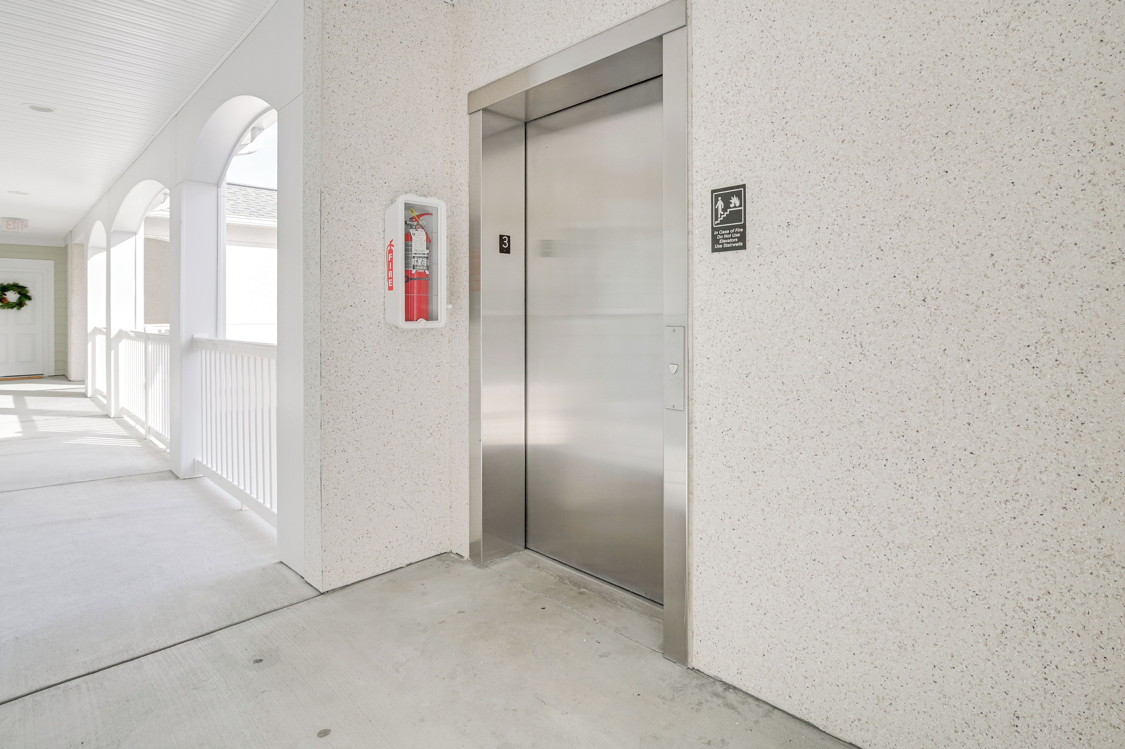 A hallway with a closed elevator, a fire extinguisher, and a door with a number plate.