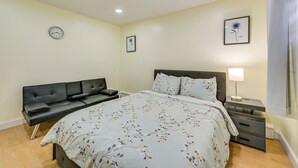 A bedroom with a bed, a black sofa, a bedside table with a lamp, and a clock on the wall. - Stay & Play in Jersey City! Walk to Path & Park (Jersey City)