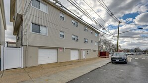 A multi-story building with a garage door, a sidewalk, and a parked car. - Stay & Play in Jersey City! Walk to Path & Park (Jersey City)