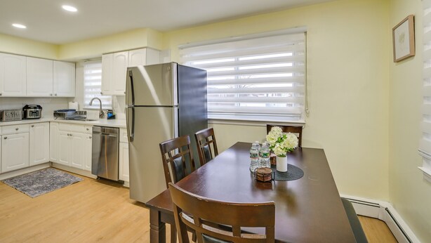 A modern kitchen with white cabinets, a stainless steel refrigerator, and a dining table with chairs. - Stay & Play in Jersey City! Walk to Path & Park (Jersey City)