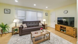 A living room with a brown sofa, a wooden coffee table, a TV on a wooden stand, and a window with blinds. - Stay & Play in Jersey City! Walk to Path & Park (Jersey City)