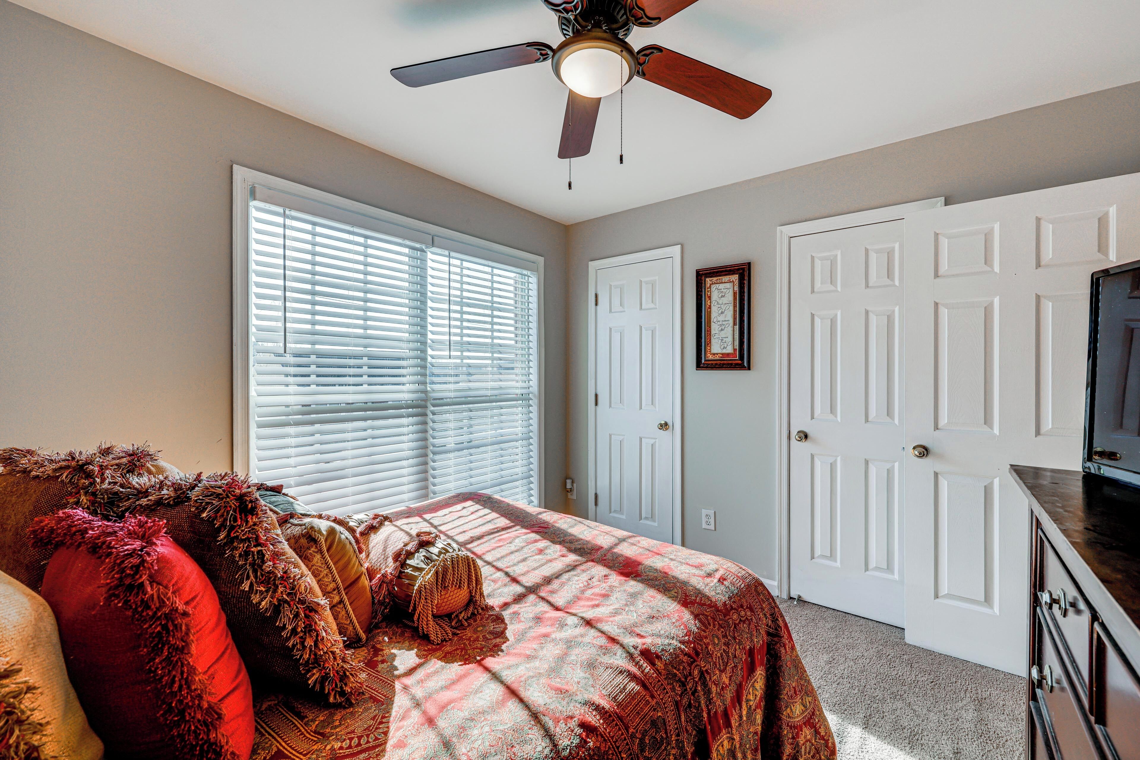 A bedroom with a bed, a ceiling fan, a dresser, and a television.