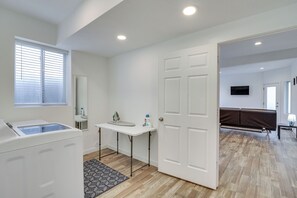 A clean, modern bathroom with a washing machine, a small table with toiletries, and a window with blinds. - Stunning Peak Views Near Utah Lake! Cozy Getaway (Orem)