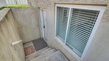 A concrete stairway leading to a door, a window with blinds, and a small patch of grass visible through a fence.
