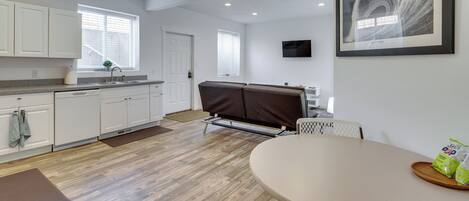 A modern kitchen with white cabinets, a dining area with a table and chairs, and a framed artwork on the wall.