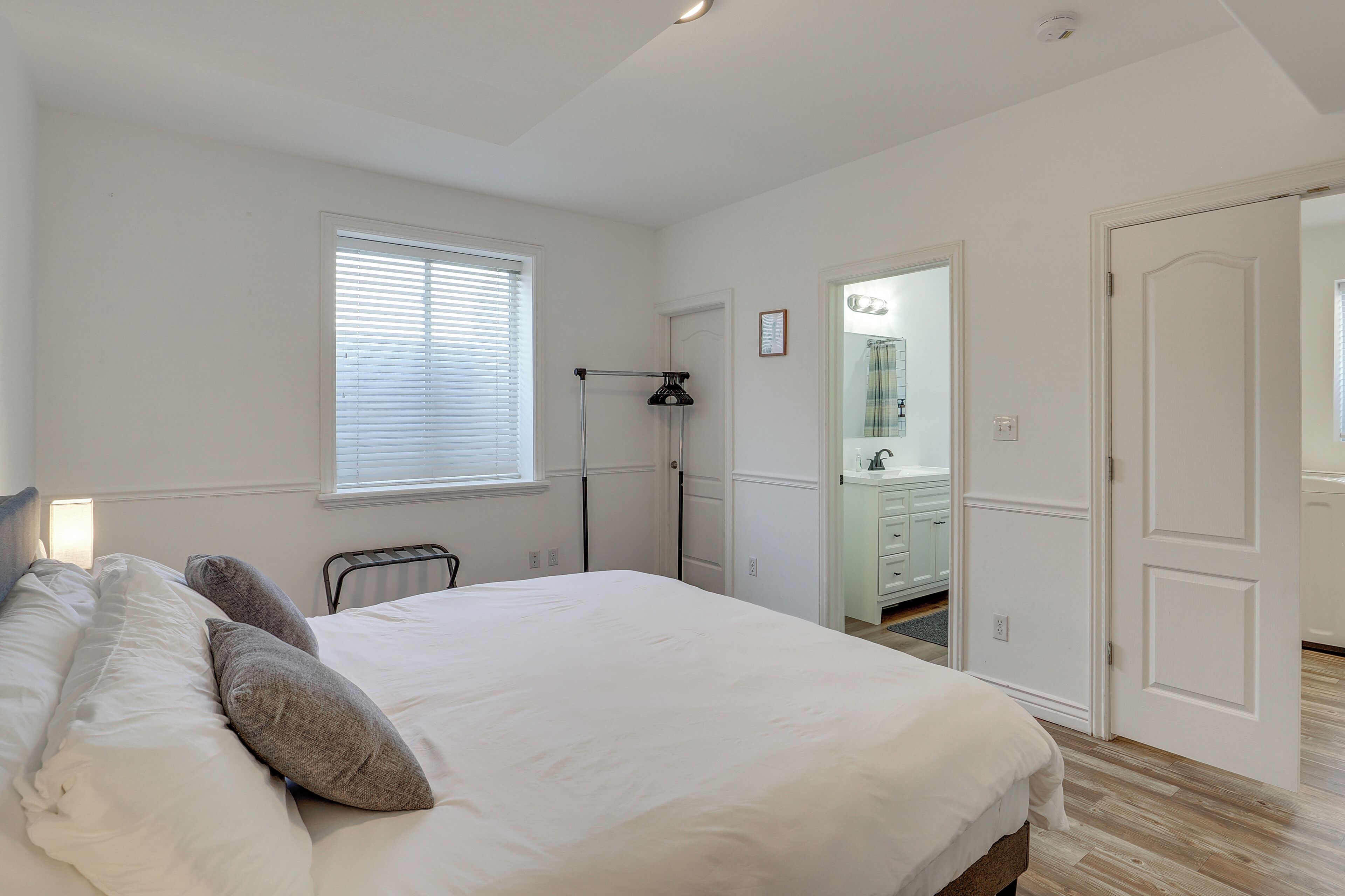 Een slaapkamer met een groot bed, een nachtkastje, een lamp en een raam met jaloezieën.
