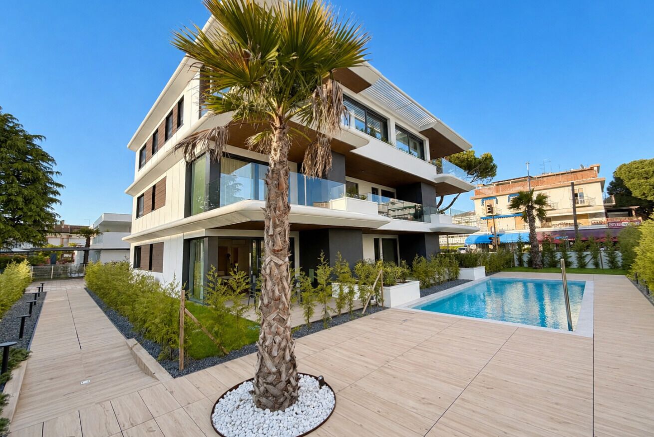 A modern multi-story building with a swimming pool, surrounded by a wooden deck and greenery.