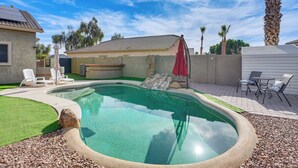 A swimming pool with a stone edge, a patio with chairs, and a covered seating area. - Heated Pool, Pets Welcome: Surprise Snowbird Haven (Surprise)