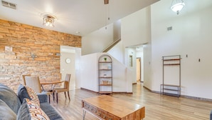 A spacious living room with a stone wall, wooden flooring, a sofa, a coffee table, and a staircase leading to another level. - Heated Pool, Pets Welcome: Surprise Snowbird Haven (Surprise)