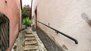 A narrow stone staircase with a metal handrail, flanked by buildings with pink and white walls. - Gîte Baumann Rombach le Franc – Cozy House with Terrace (Rombach le Franc)