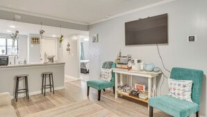 Una cocina moderna con barra, una mesa de comedor con sillas y una sala de estar con televisor y estantería.