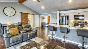 A modern kitchen with stainless steel appliances, a bar area with stools, and a dining area with a leather couch and a rug. - Private Dock at Ozarks Home Next to Margaritaville (Osage Beach)