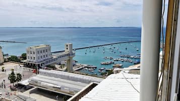 Un paisaje urbano costero con un puerto lleno de barcos, un edificio blanco destacado con una torre, y un puente peatonal sobre el agua.