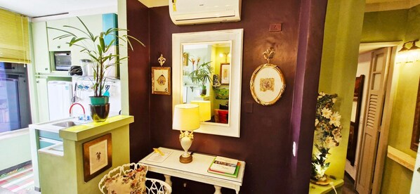 A room with a mirror, a small table with a lamp, a potted plant, and a framed picture on the wall. - COPSE0103 - Edifício Themis (Salvador)