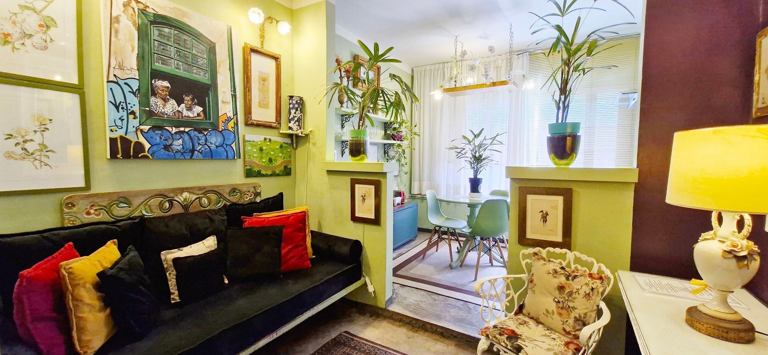 Uma sala de estar aconchegante com um sofá de cor escura, uma mesa de jantar com cadeiras e diversas obras de arte emolduradas nas paredes.