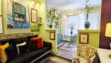 Una sala de estar acogedora con un sofá de color oscuro, una mesa de comedor con sillas y varias obras de arte enmarcadas en las paredes.