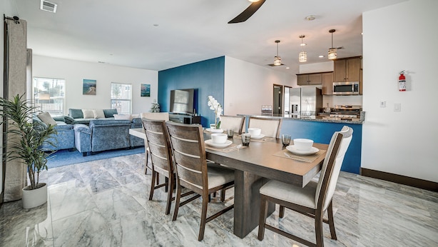 A modern living room with a blue accent wall, a dining area with a marble floor, and a kitchen with wooden cabinets and stainless steel appliances. - Fully Updated! Prime Riverside Spot Near Dtwn (Riverside)