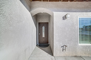 Una casa con puerta marrón, un pequeño porche y una ventana con persianas.