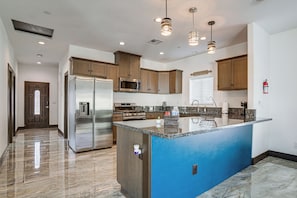 Una cocina moderna con una isla central, electrodomésticos de acero inoxidable, armarios de madera e iluminación colgante.
