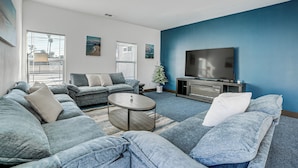 A modern living room with a sectional sofa, a coffee table, and a flat-screen TV against a blue accent wall. - Fully Updated! Prime Riverside Spot Near Dtwn (Riverside)