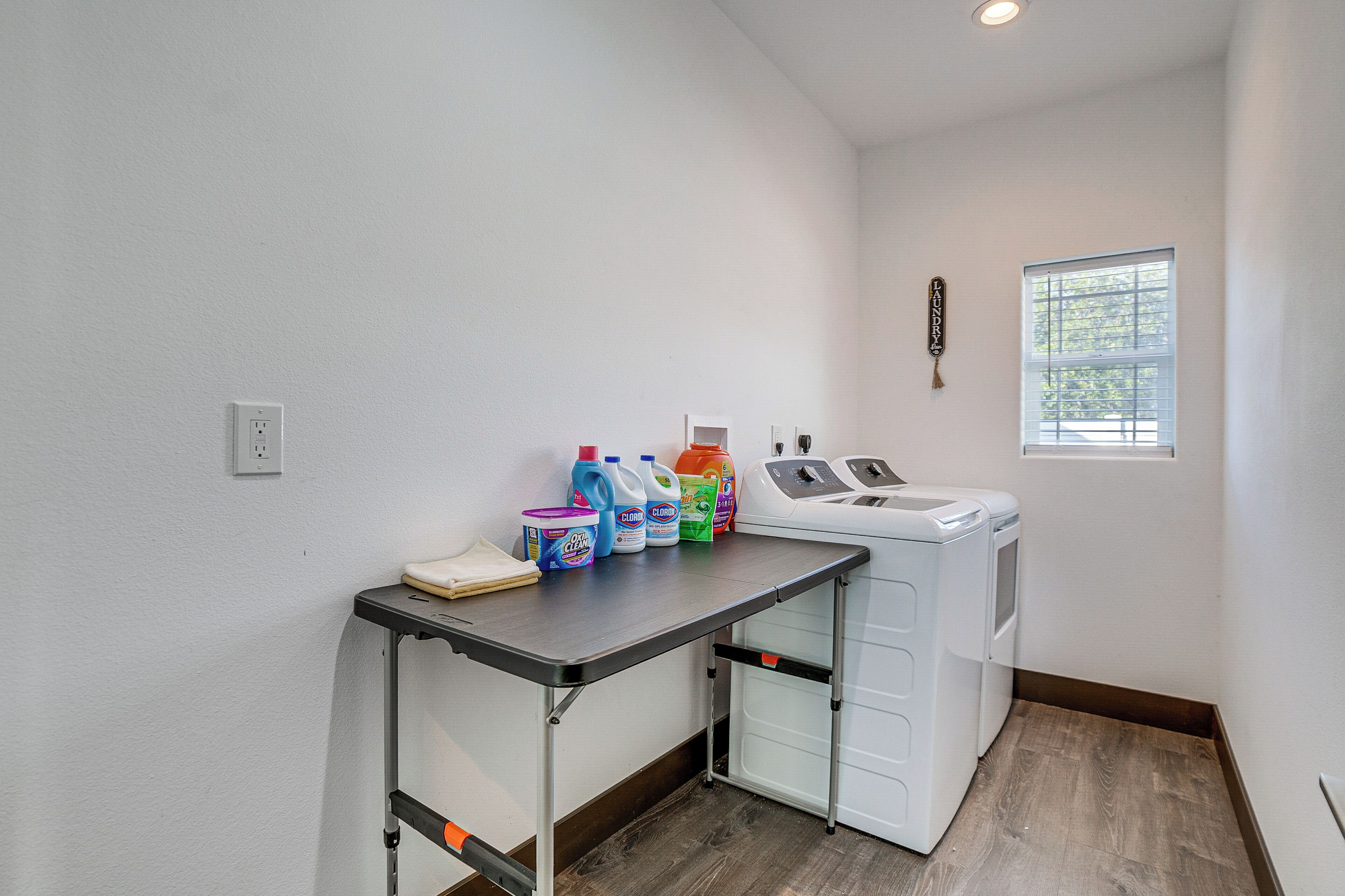 A laundry room with a washing machine, dryer, and a table with various cleaning products.