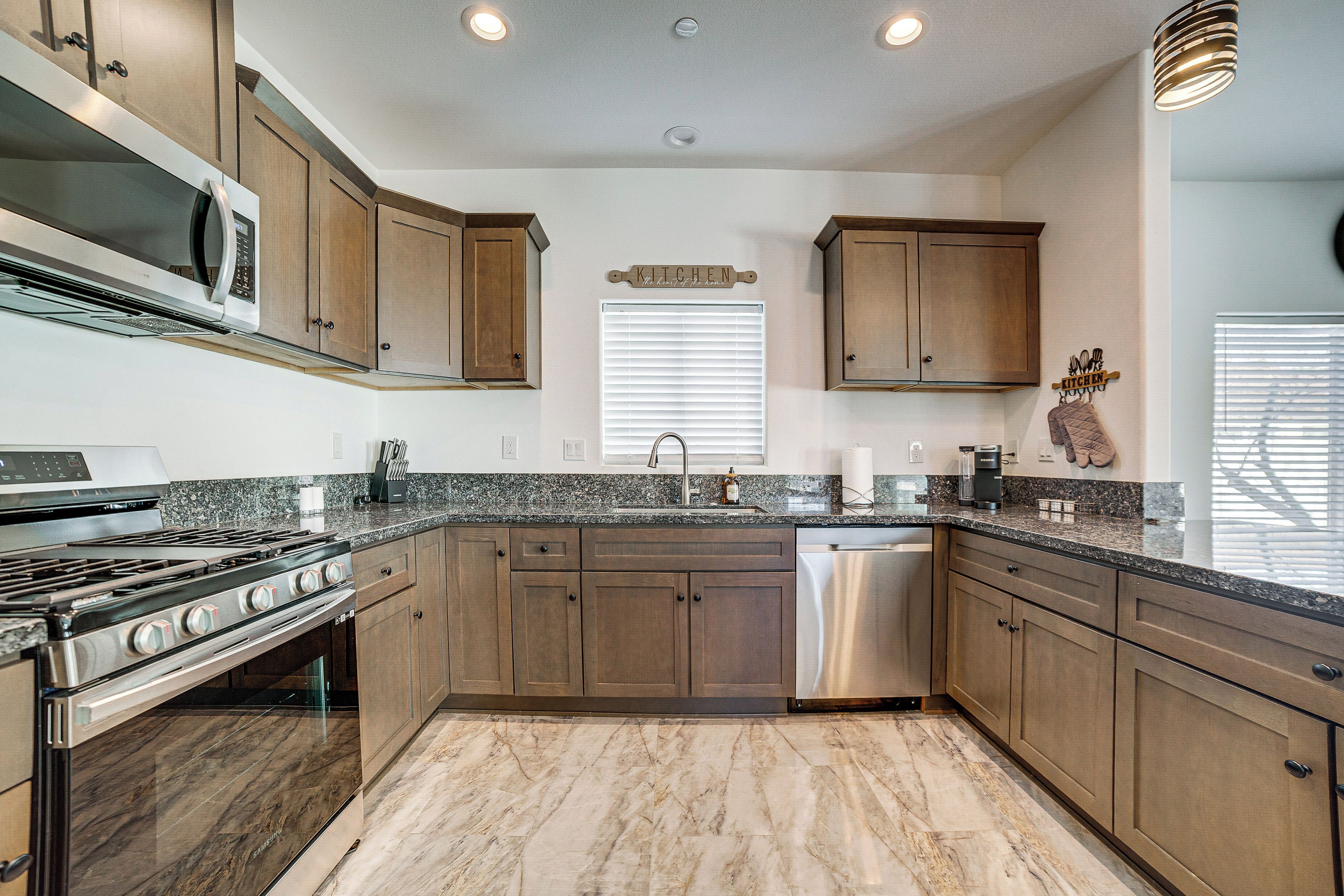 A modern kitchen with granite countertops, stainless steel appliances, wooden cabinets, and a marble floor.