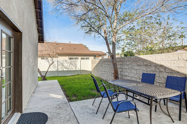 An outdoor patio with a table and chairs, a stone wall, and a grassy area.