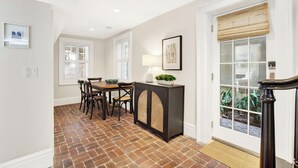 A dining area with a brick floor, a table with chairs, a cabinet, and a door with a window. - Hidden Garden Retreat in the Heart of Downtown Savannah (savannah)