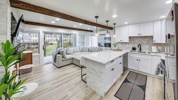 A modern kitchen with white cabinetry, a large island, and a dining area with a gray sectional sofa. - Seasonal Pool & Marina! Condo on Lake Pend Oreille (Sandpoint)