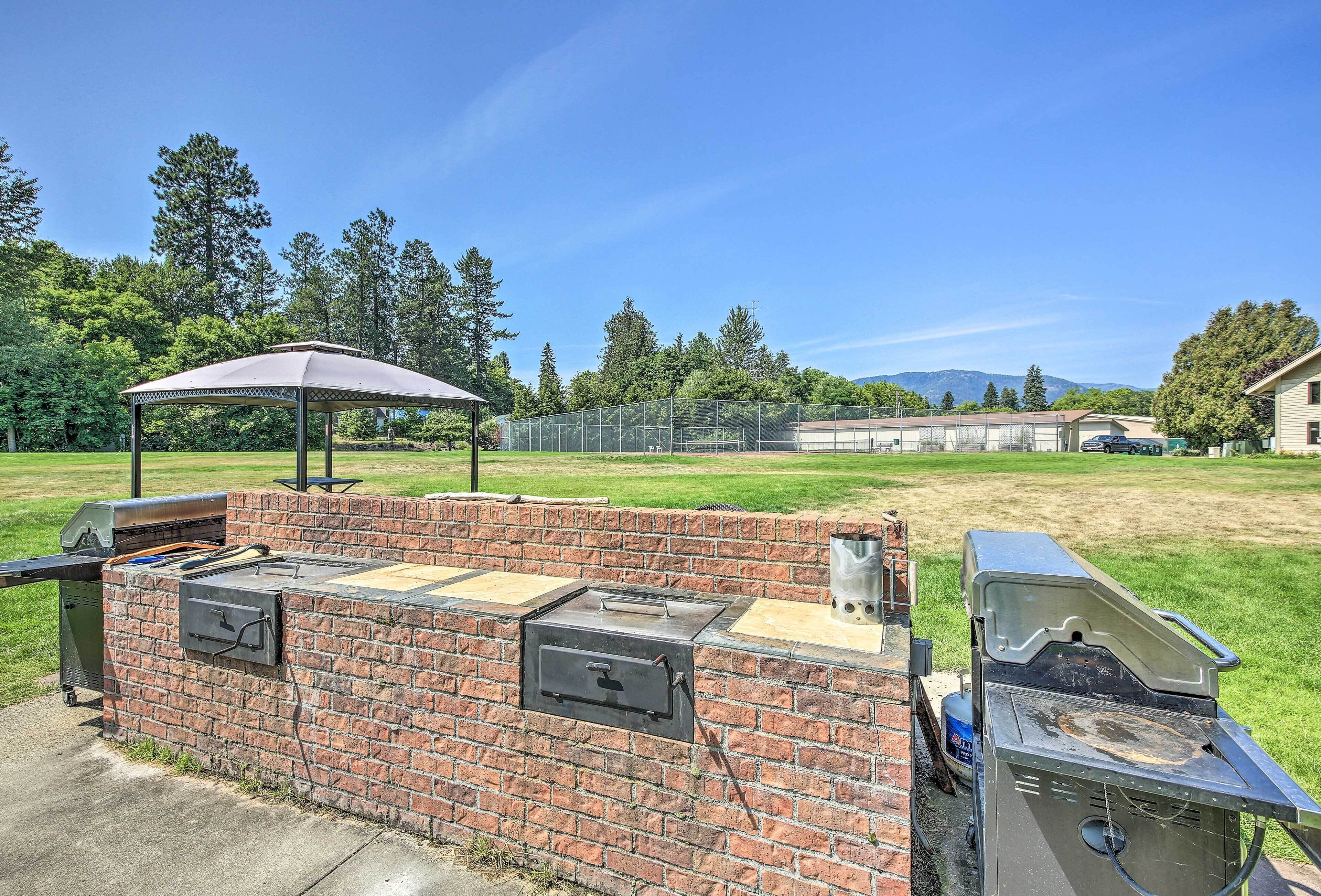 A brick barbecue grill with a chimney, a grill cover, and a portable gas grill.