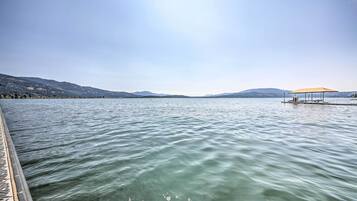 A calm lake with a wooden dock extending into the water, a small pavilion with a canopy, and distant mountains under a clear sky.