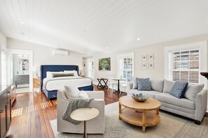 Ein modernes, helles Wohnzimmer mit einem großen Bett, einer Couch, einem Couchtisch und einem Essbereich.