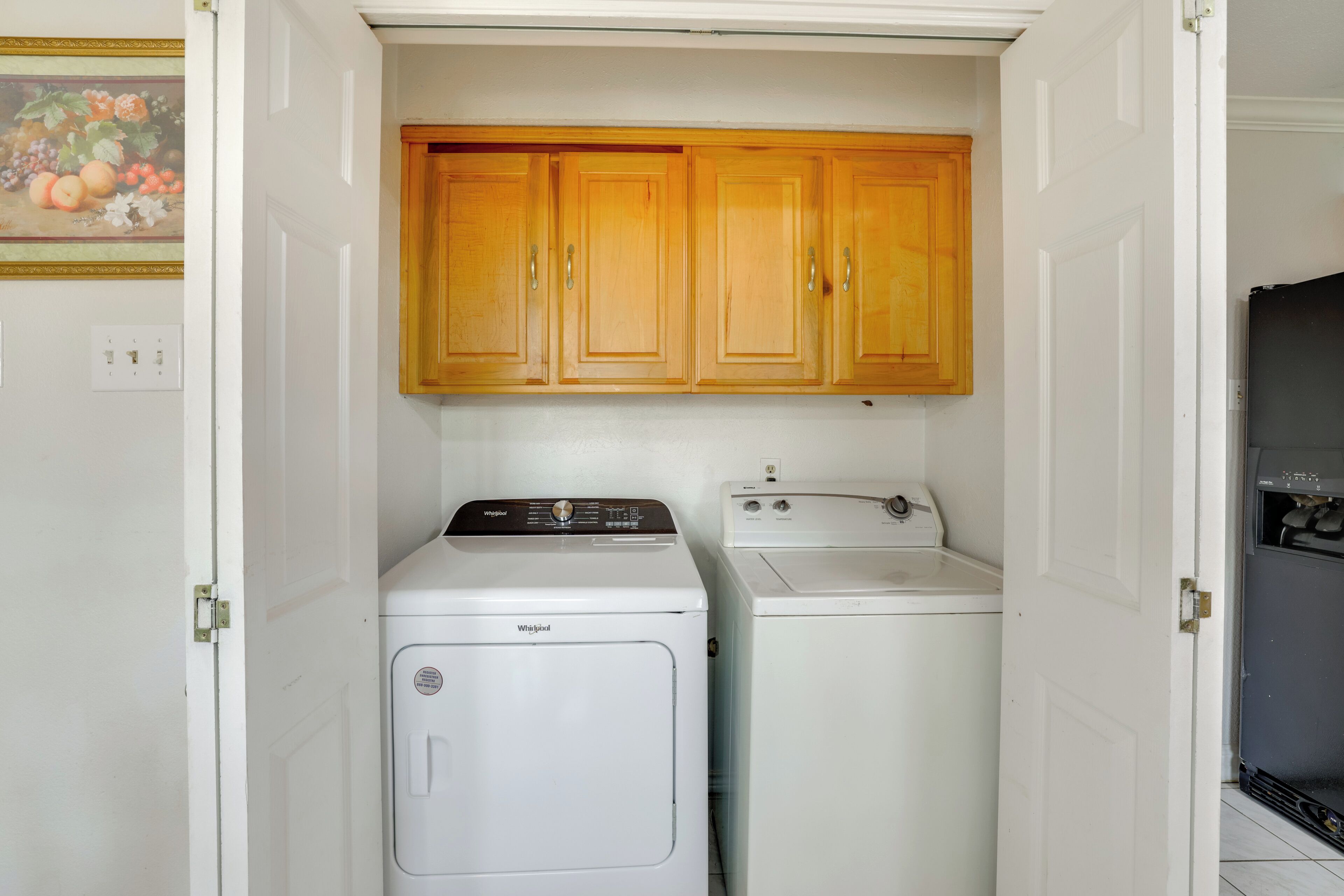 Uma lavanderia com duas máquinas de lavar Whirlpool brancas e armários de madeira acima.