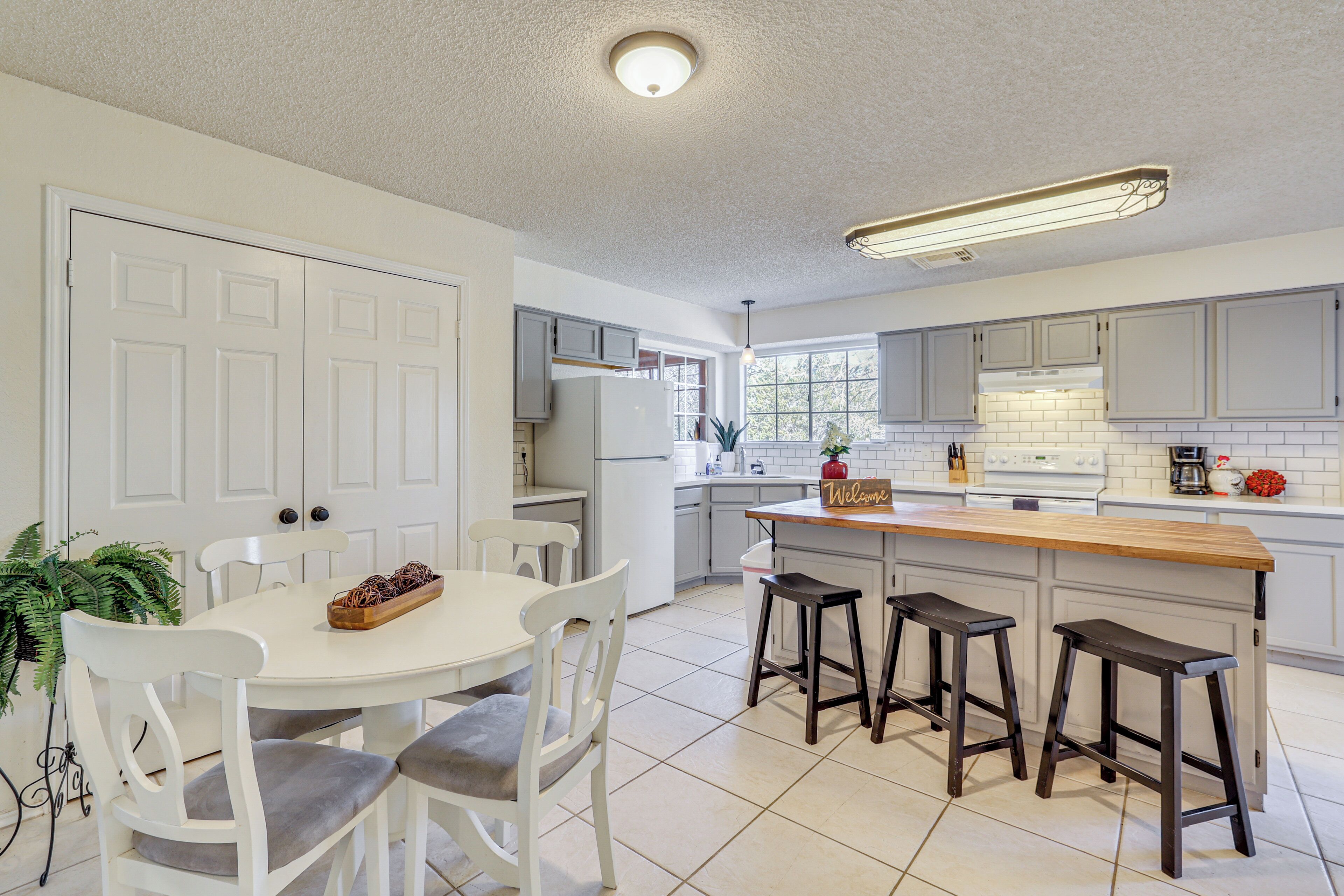 A modern kitchen with white cabinetry, a wooden island, and bar stools.