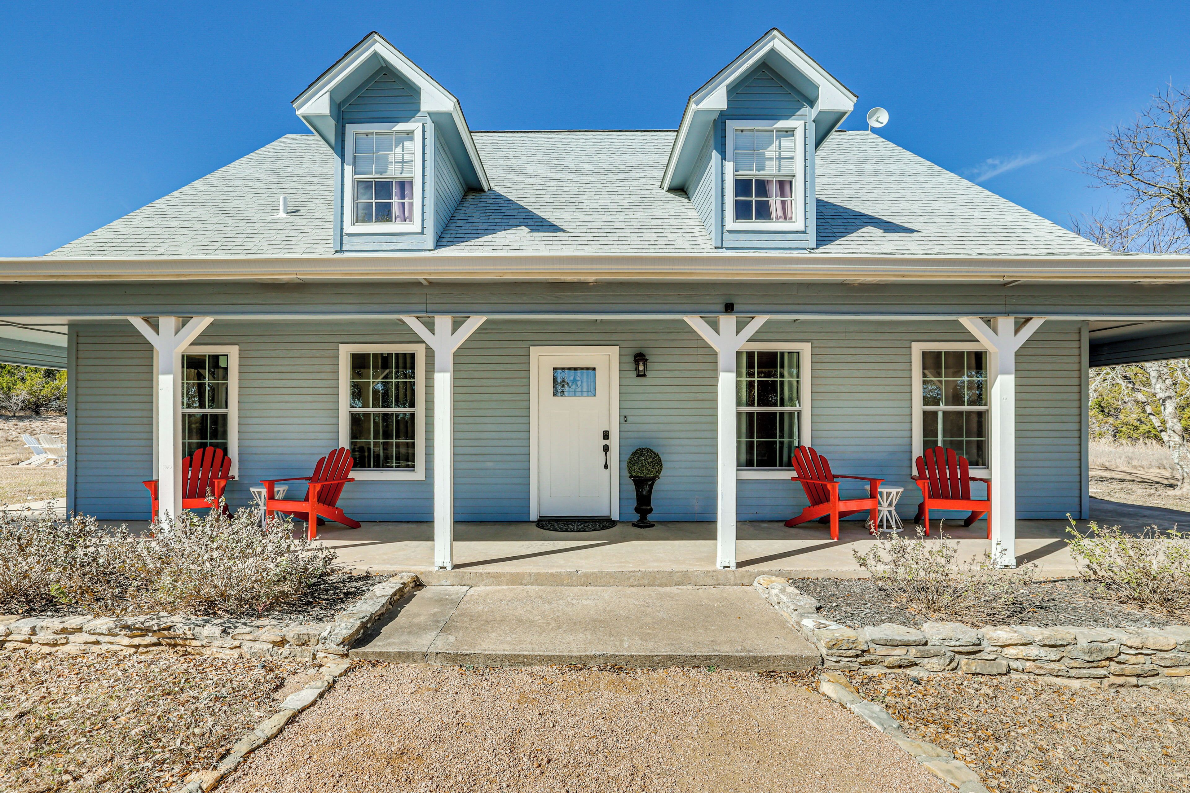 A two-story house with a covered porch, two red Adirondack chairs, and a stone pathway leading to the door.