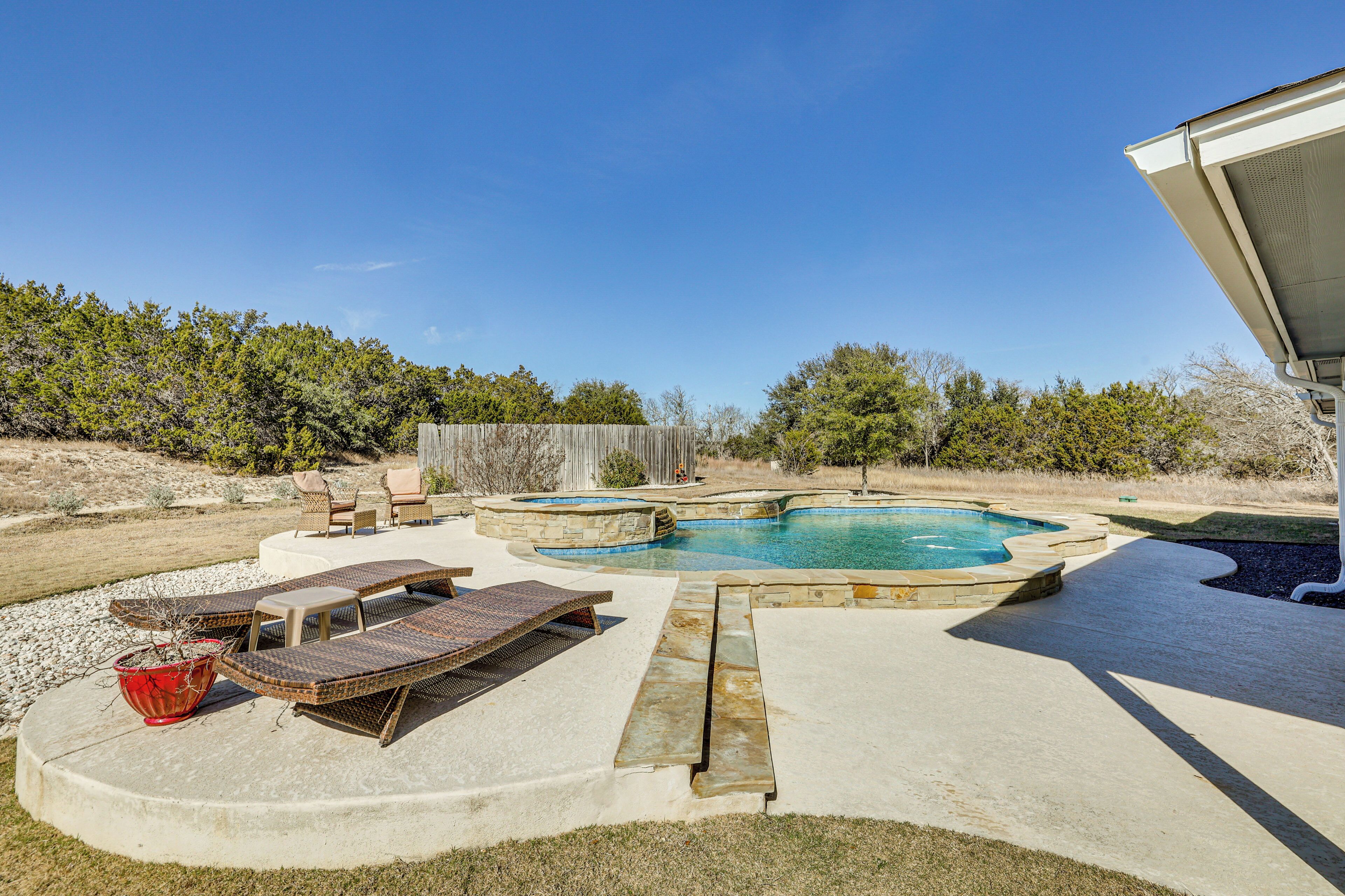 A backyard with a swimming pool, lounge chairs, and a fire pit.