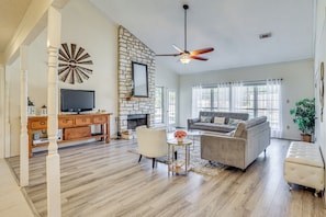 A spacious living room with a fireplace, a large TV, and a ceiling fan. - Hill Country Escape: Family Home w/ Outdoor Oasis (Dripping Springs)