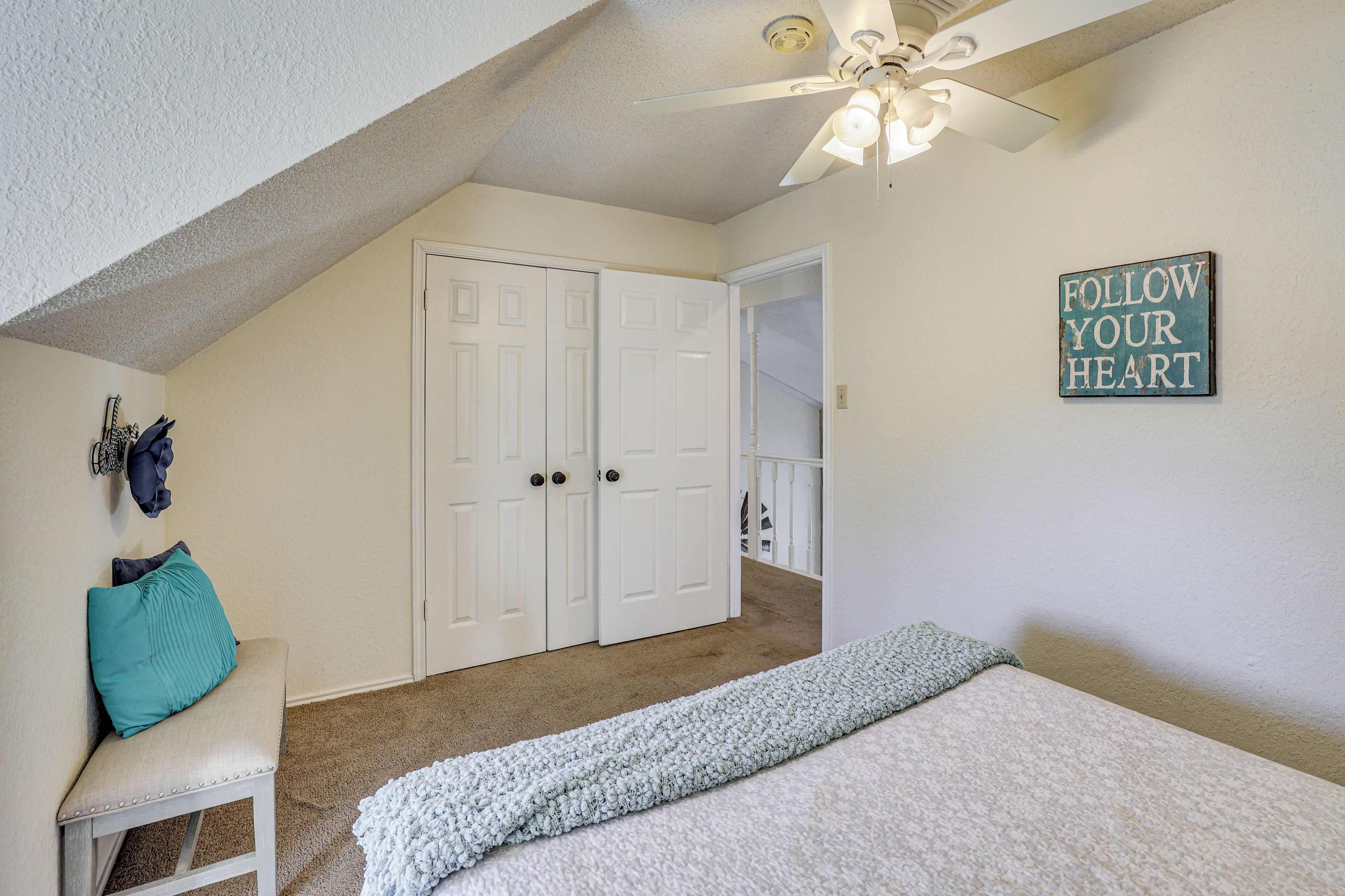 A bedroom with a bed, a bench, a ceiling fan, and a door.