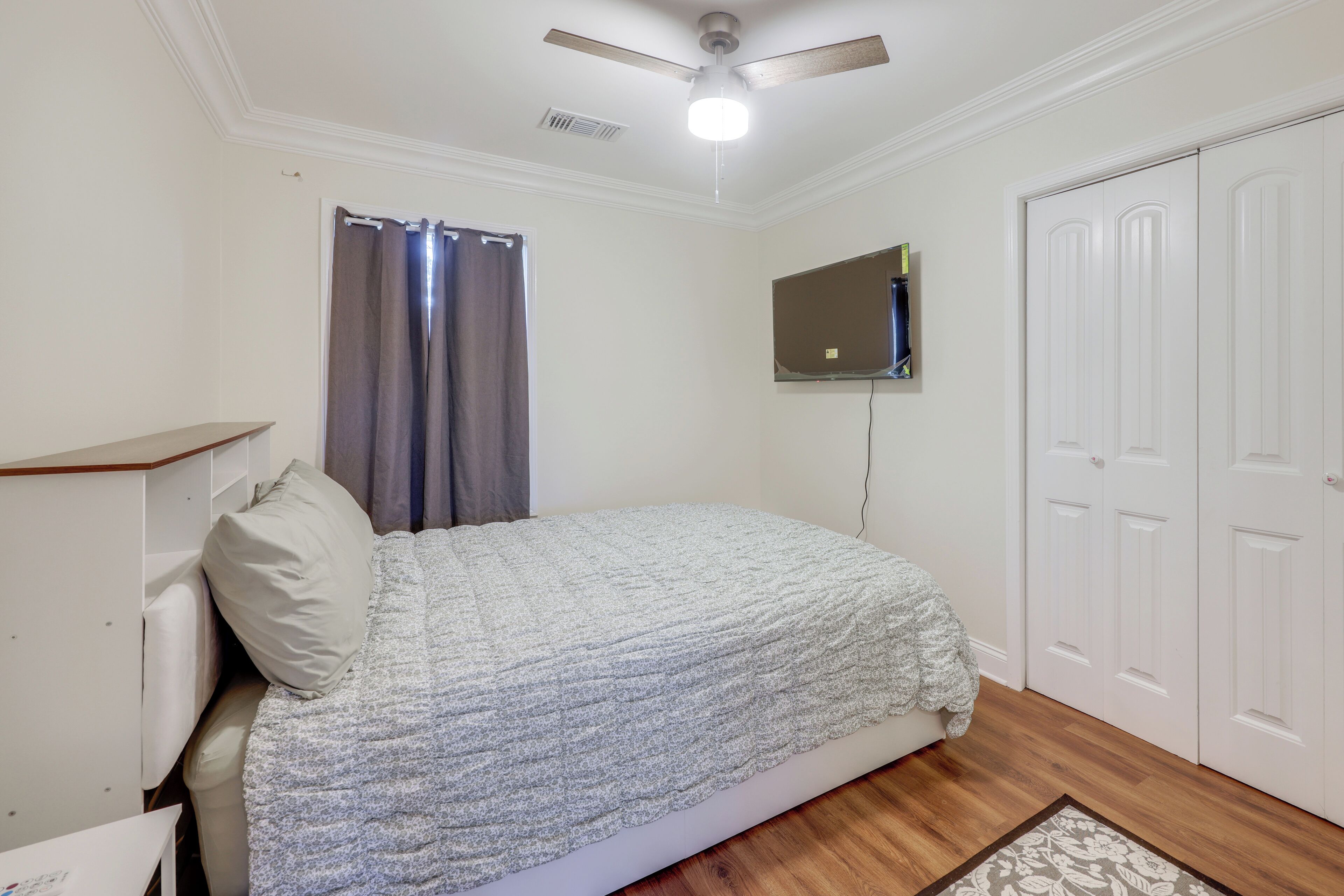 A bedroom with a bed, a ceiling fan, a TV mounted on the wall, and a wardrobe.