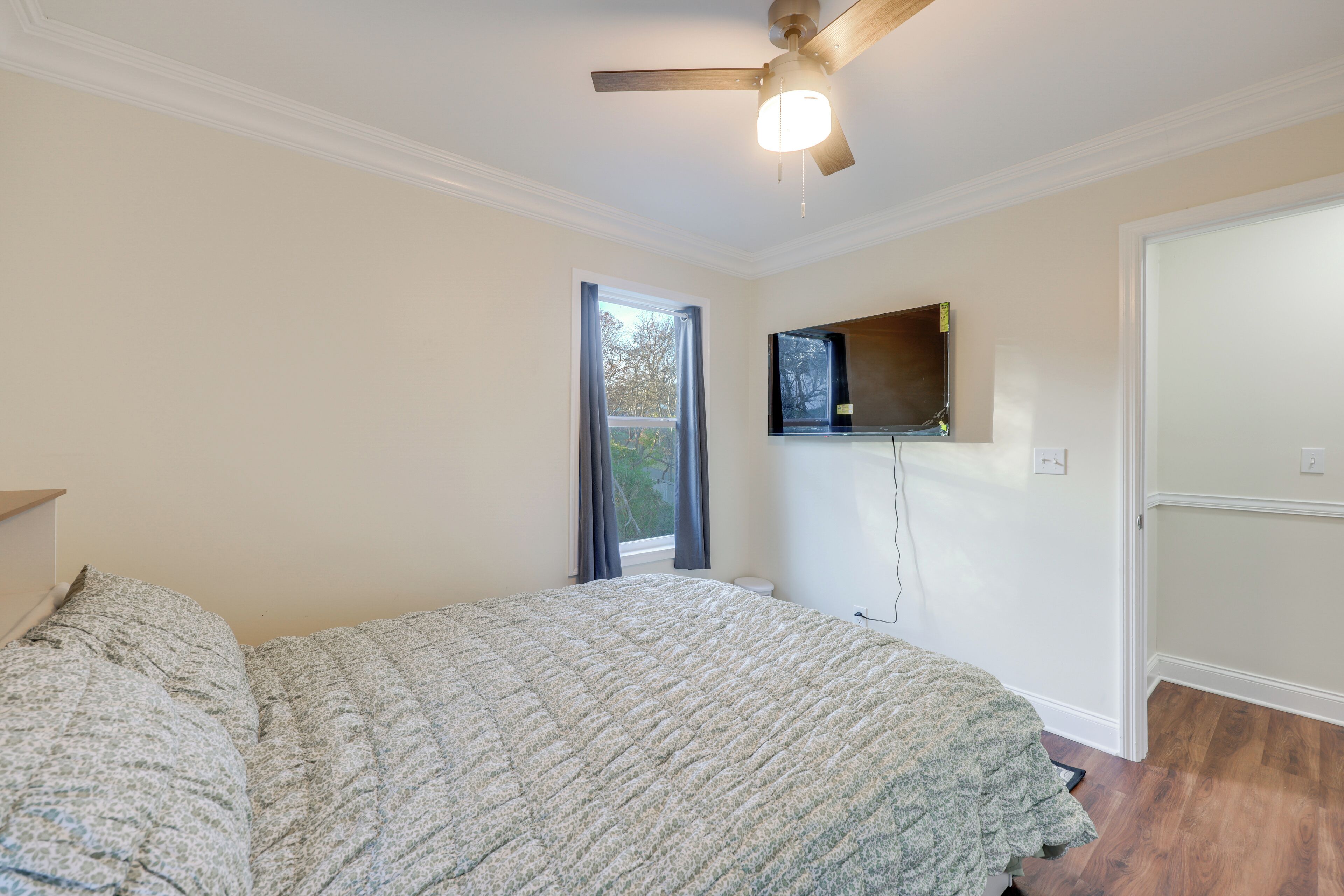 Un dormitorio con cama, ventilador de techo, ventana con cortinas y televisor de pared.