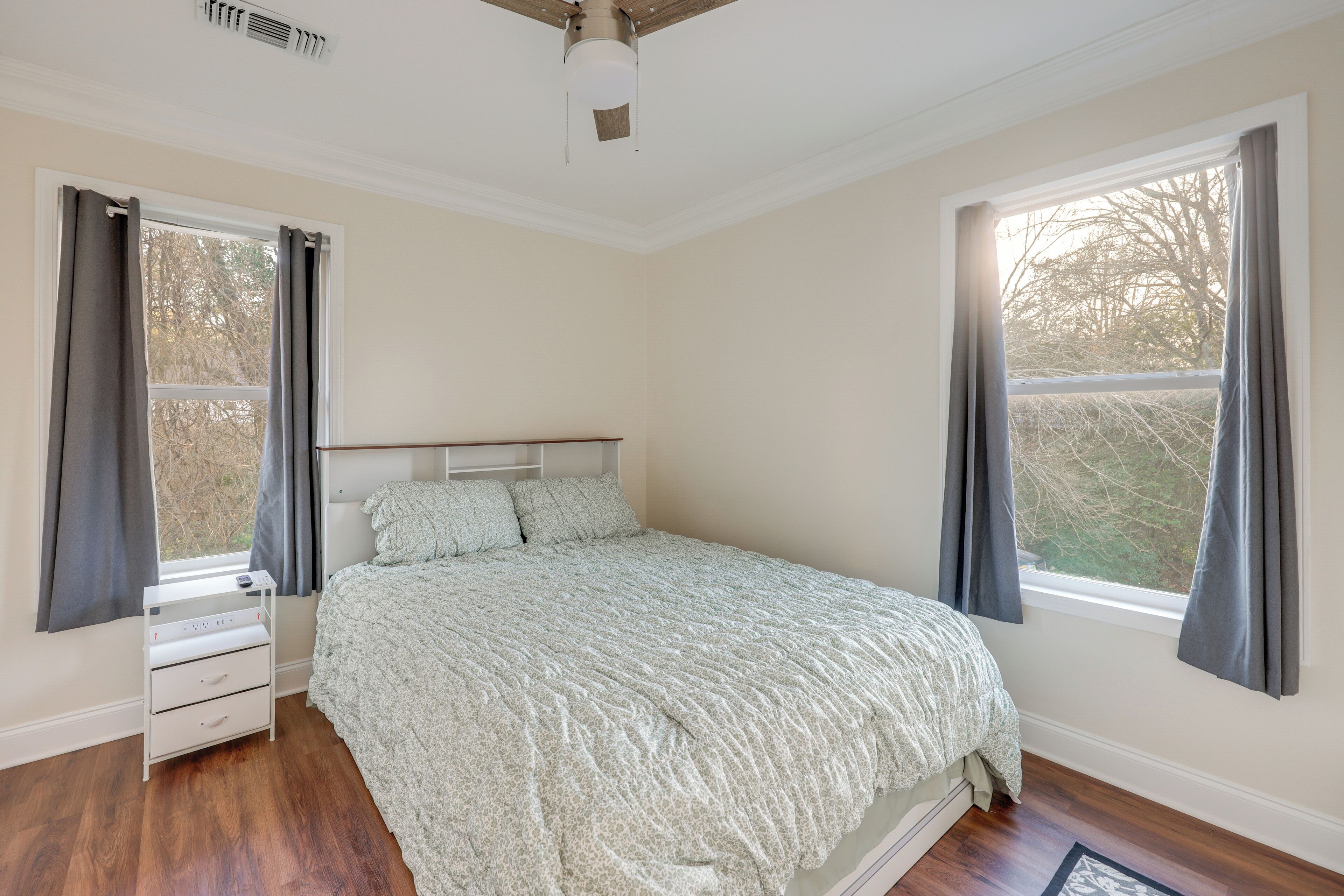 A bedroom with a bed, a nightstand, a dresser, and a window with curtains.